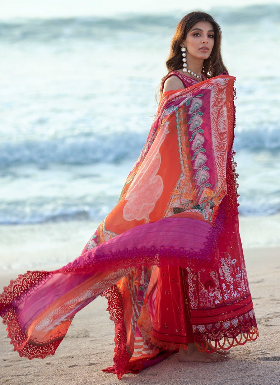 Woman in a vibrant saree standing on a beach with ocean waves in the background