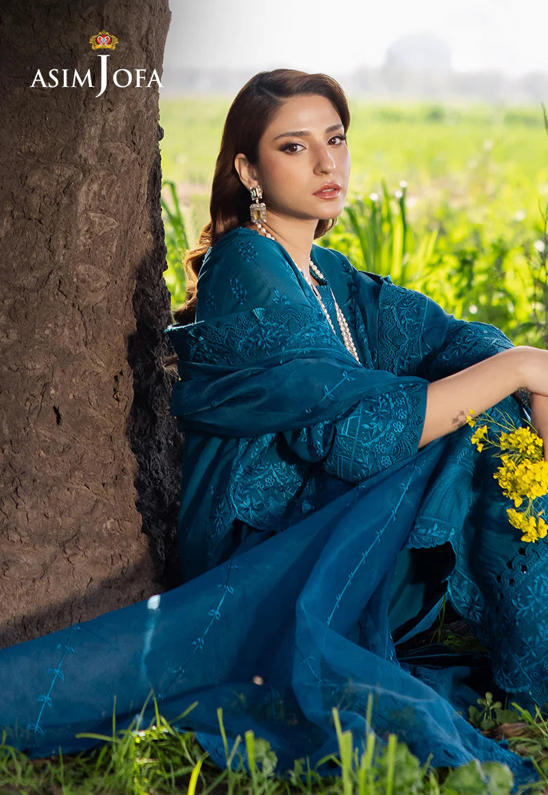 Woman in a blue traditional outfit sitting in a field with 'Asim Jofa' branding.