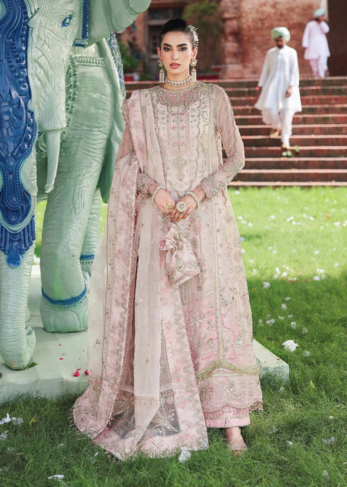 Woman in a traditional pink embroidered outfit standing in front of decorative elephants and a building.