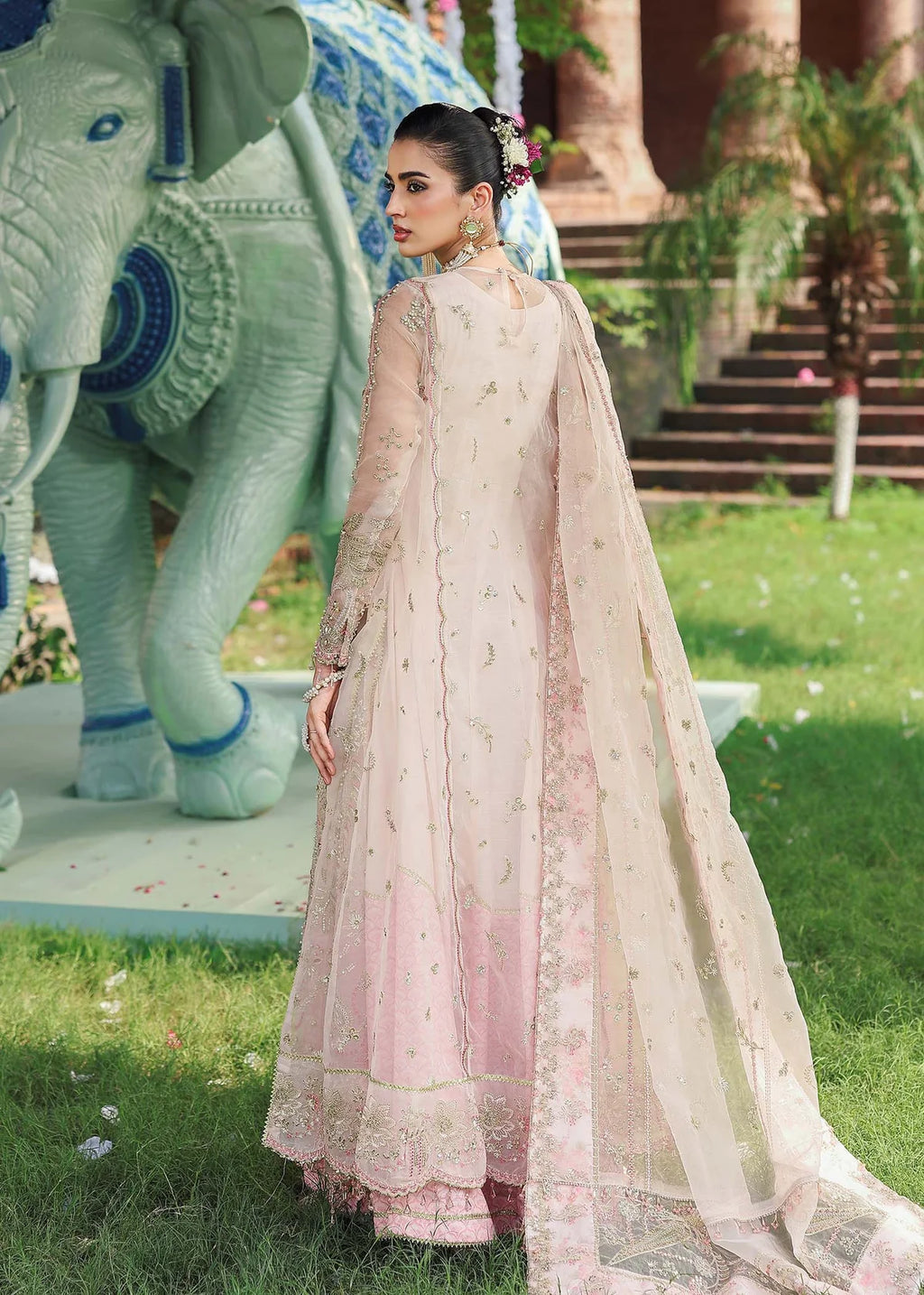 Woman in a traditional outfit standing in front of an elephant statue in a garden.
