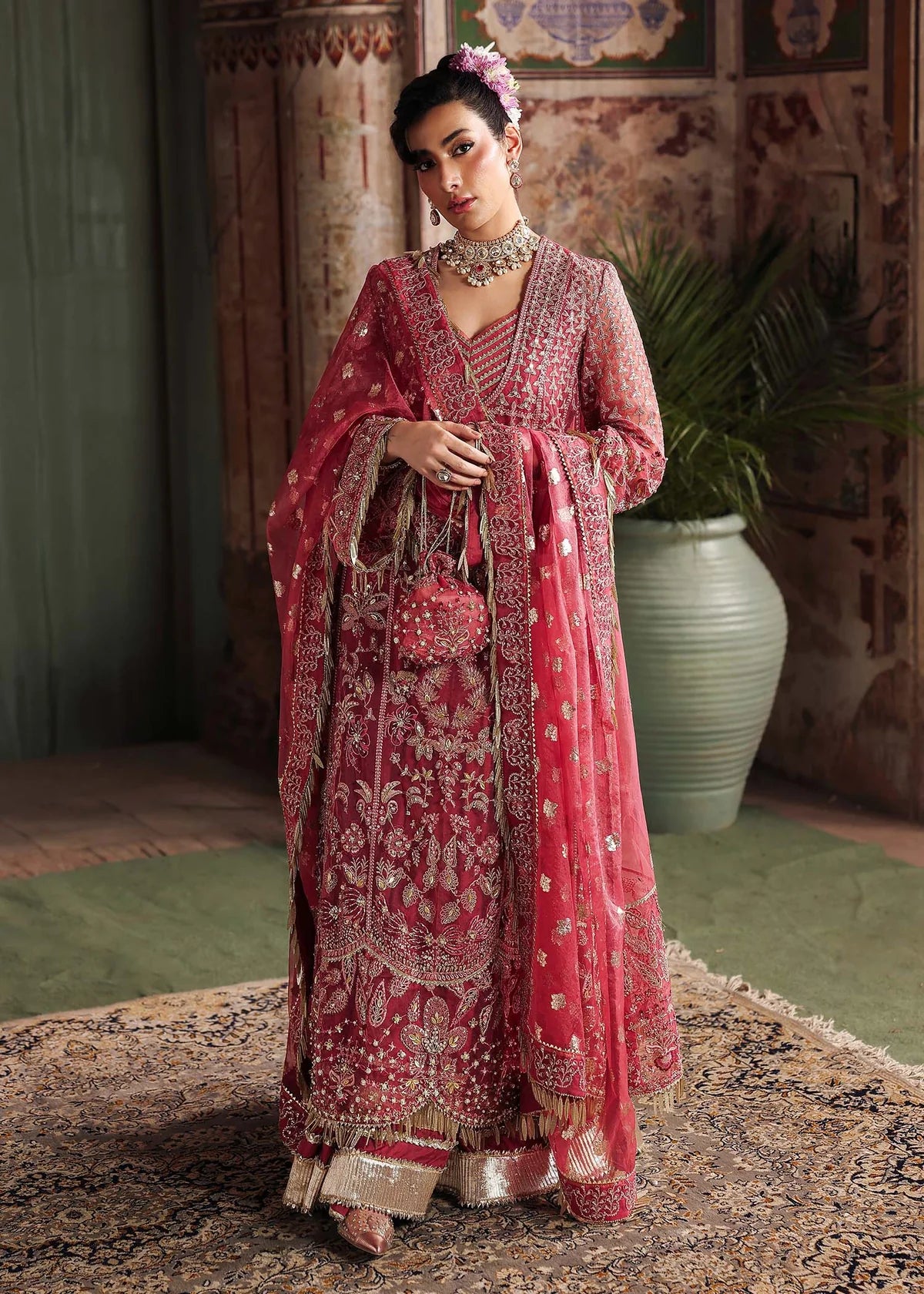 Woman in a pink embroidered traditional outfit standing in a decorated room.