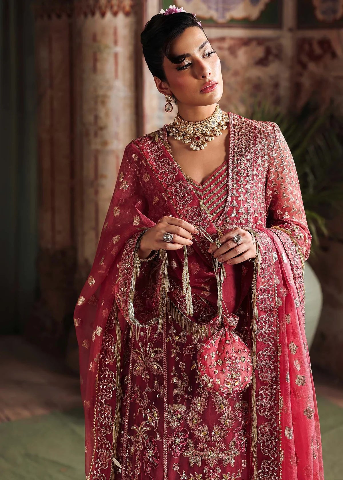 Woman in traditional pink embroidered outfit with jewelry, holding a matching bag.