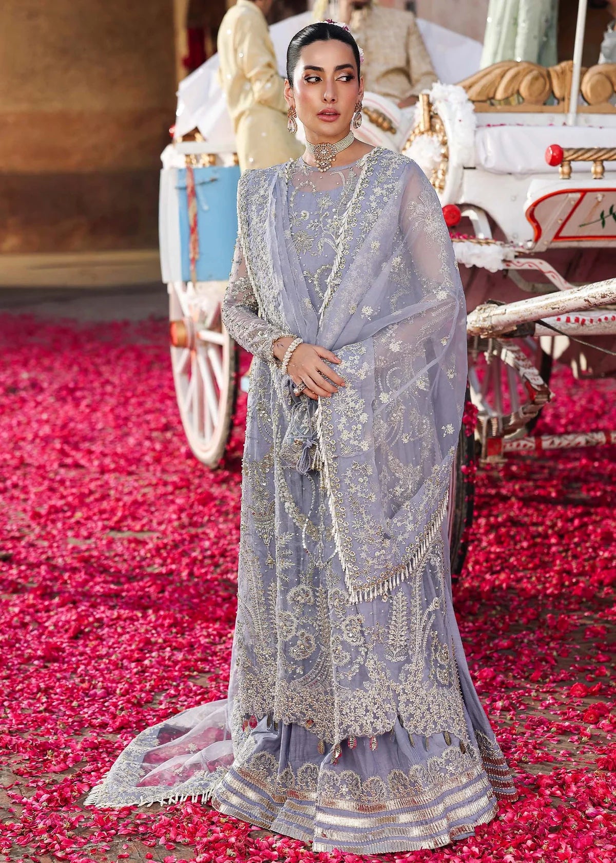 Woman in traditional embroidered outfit standing on a red carpet with decorative elements.