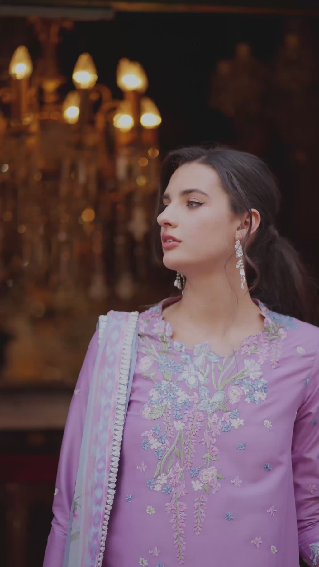 Woman in a purple embroidered outfit with a chandelier in the background