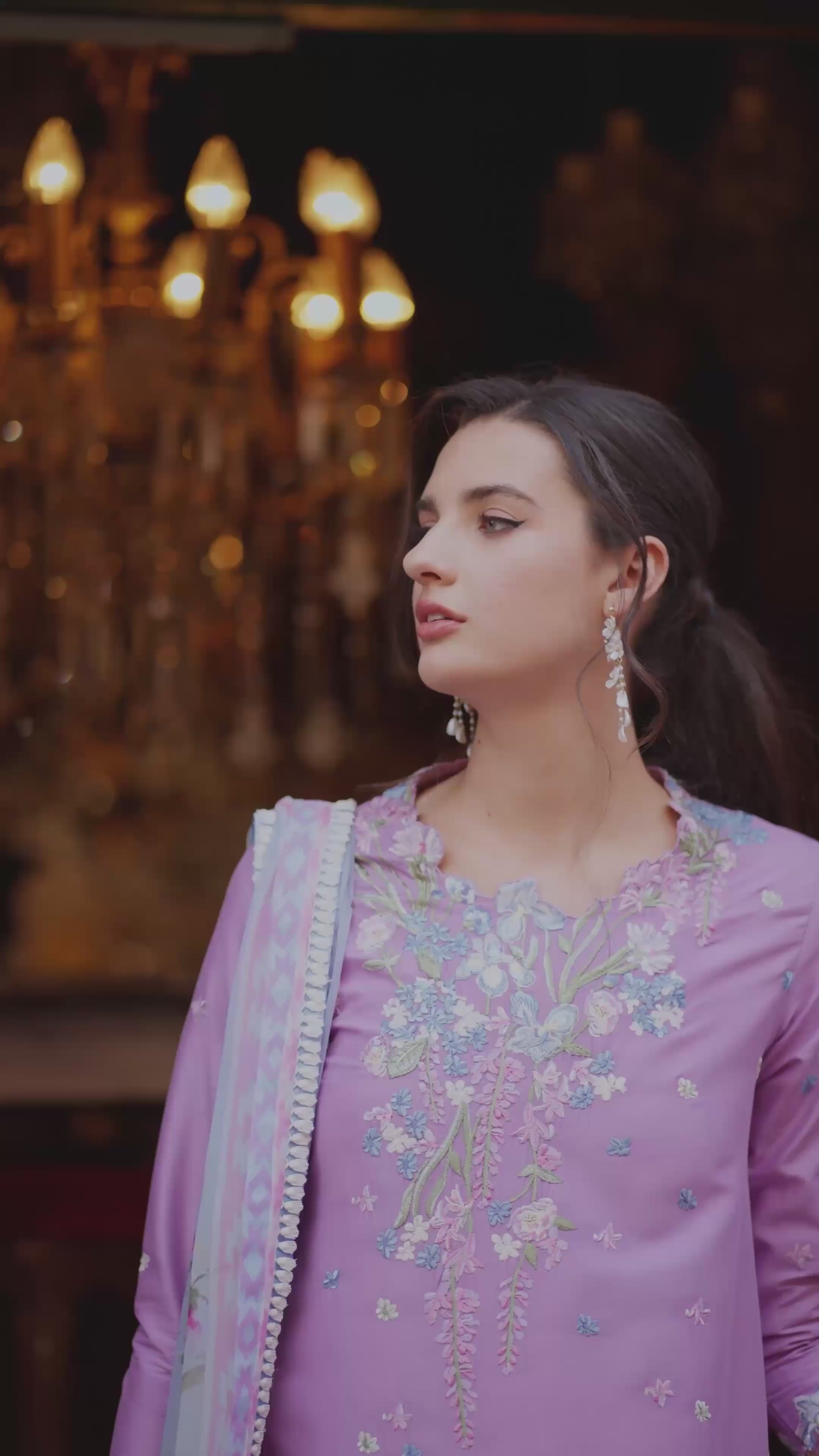 Woman in a purple embroidered outfit with a chandelier in the background