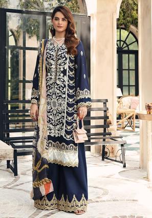 A woman models a traditional three-piece navy blue salwar kameez suit with intricate silver and gold embroidery, paired with a beige dupatta, in an outdoor courtyard setting.