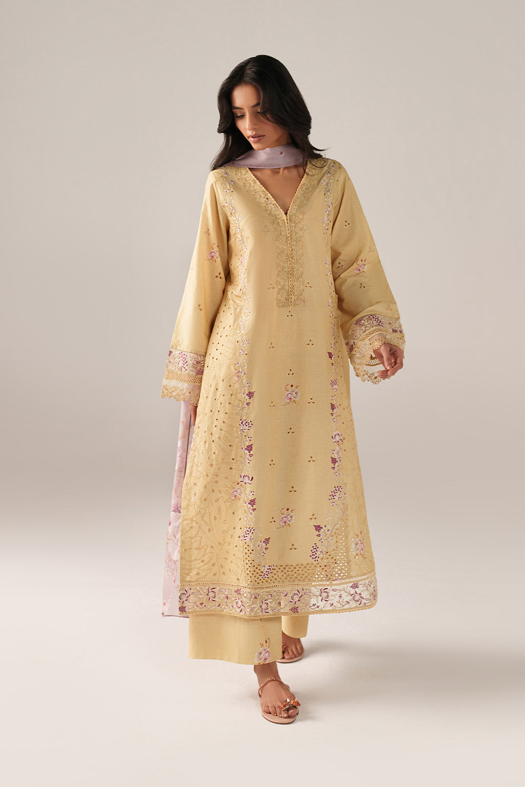 Woman wearing a light yellow embroidered kurta with palazzo pants on a plain background