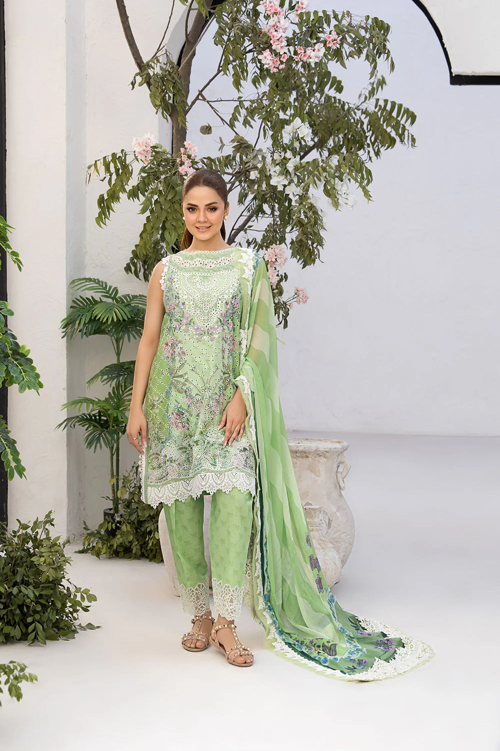 Woman in a green traditional outfit with floral patterns standing in a decorated indoor setting.