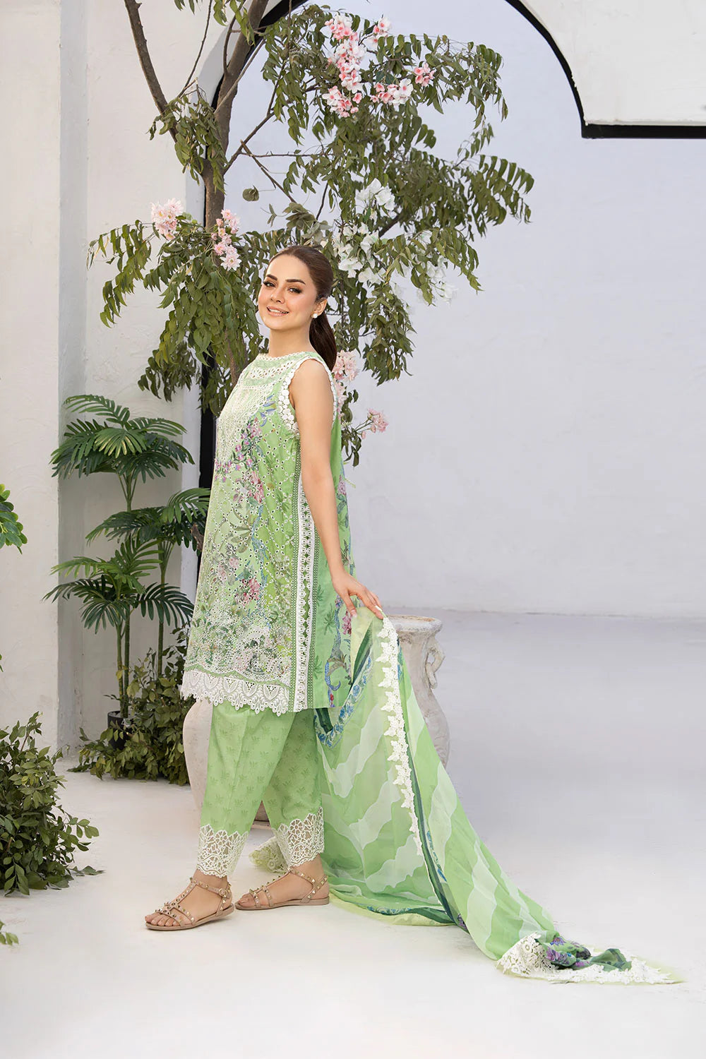 Woman in a green traditional outfit standing in front of decorative plants.