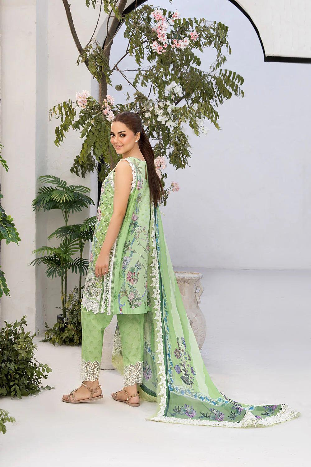 Woman in a light green traditional outfit with floral patterns standing in a decorated indoor setting.