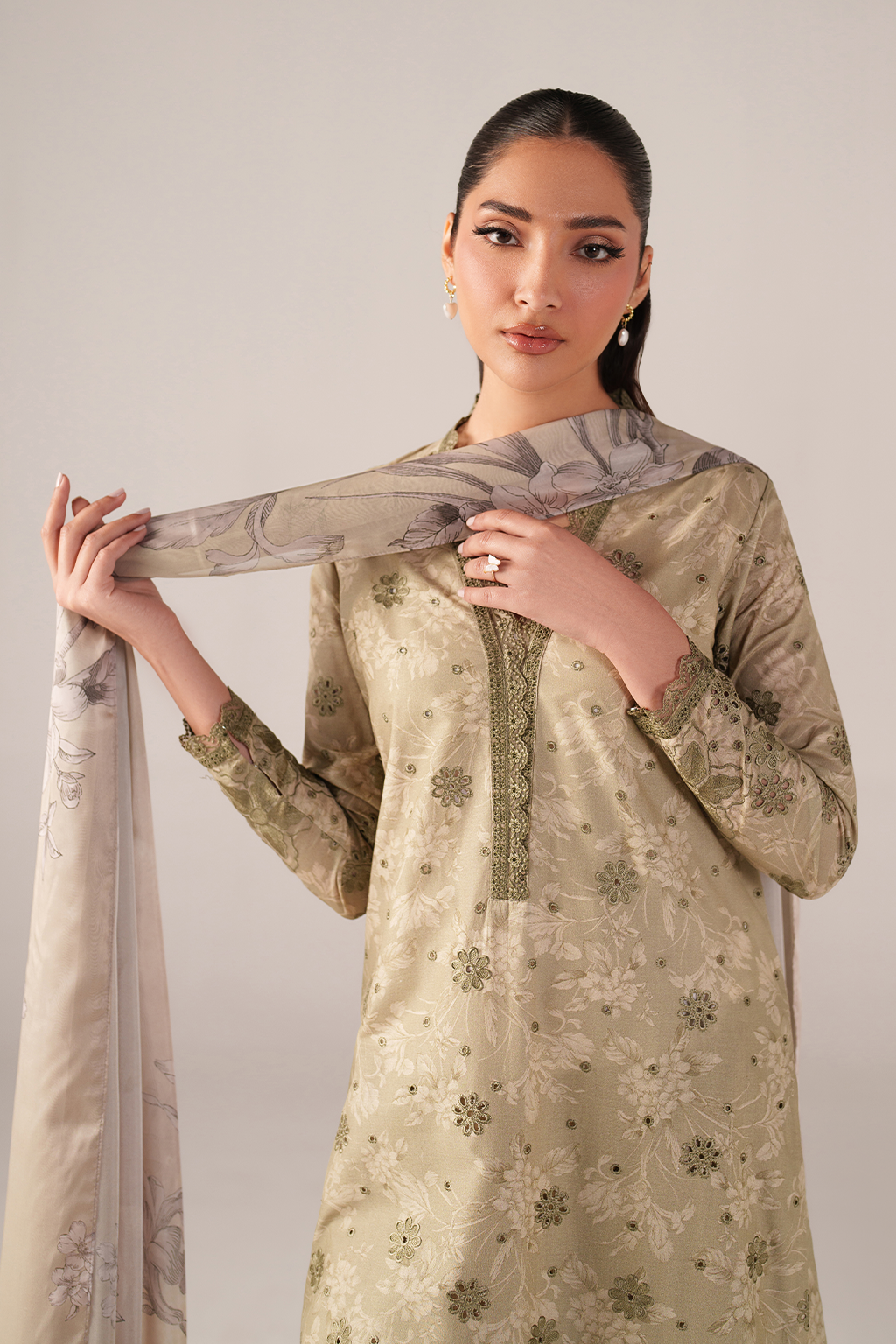 Woman wearing a beige embroidered traditional outfit with a matching dupatta against a plain background