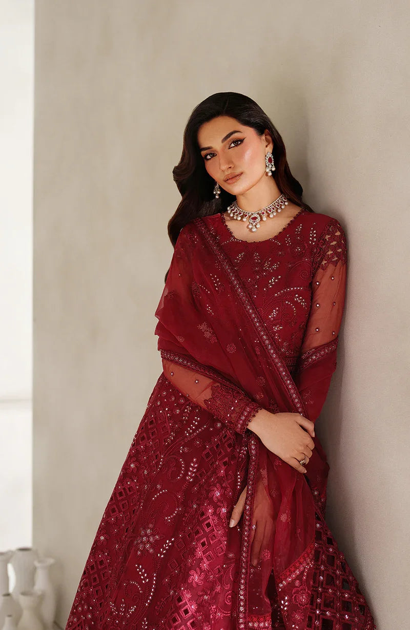 Woman wearing a red saree with intricate patterns against a neutral background