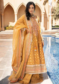A woman models a traditional Indian salwar kameez suit in mustard yellow with intricate embroidery, standing next to a swimming pool with a resort-style archway background.