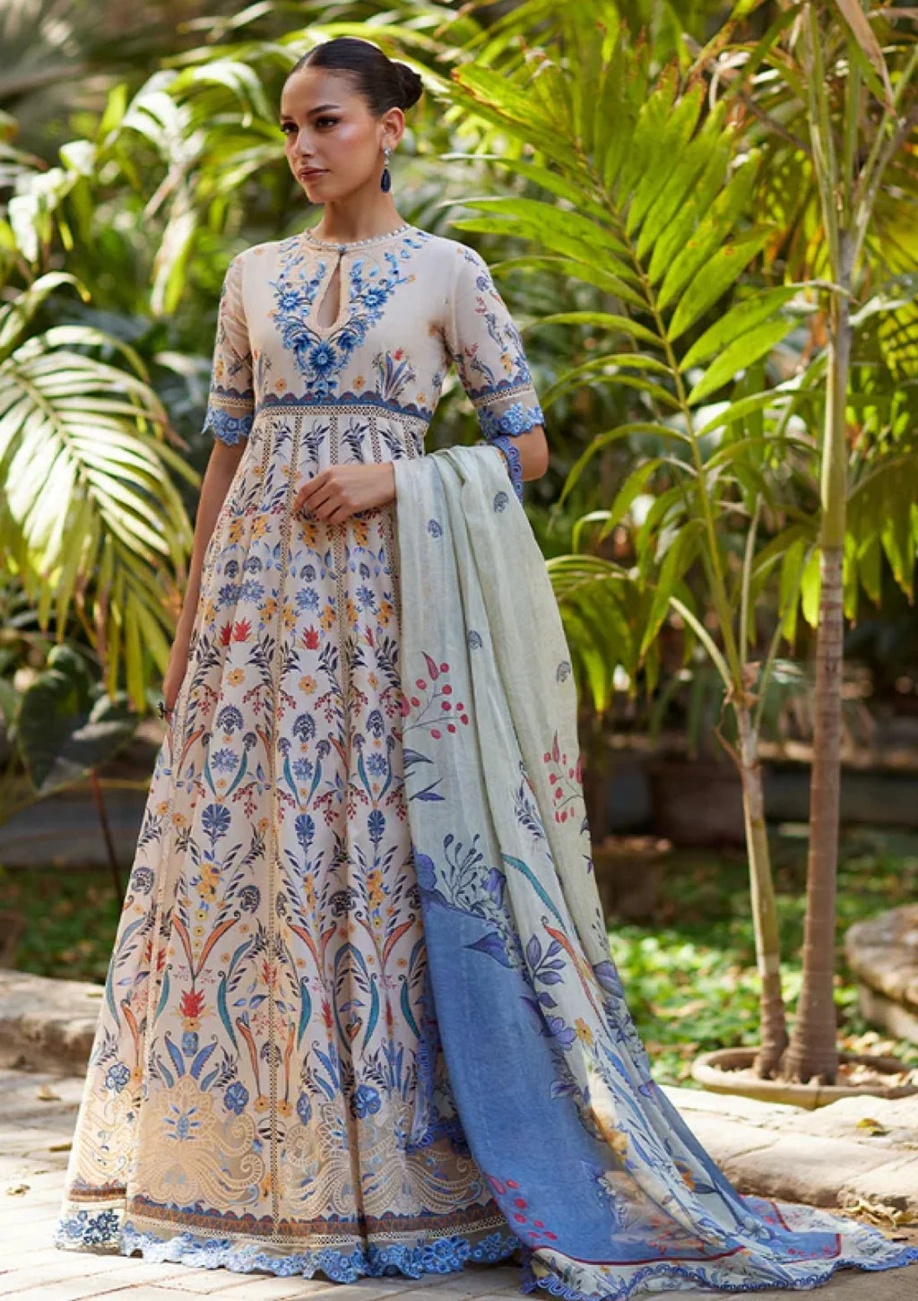 Woman in a floral dress with a blue dupatta standing in a garden.