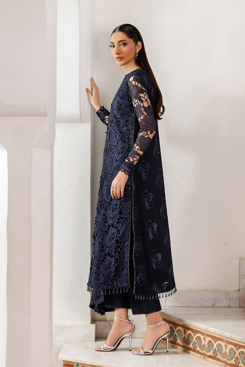 Woman wearing a navy blue lace outfit standing against a white wall.
