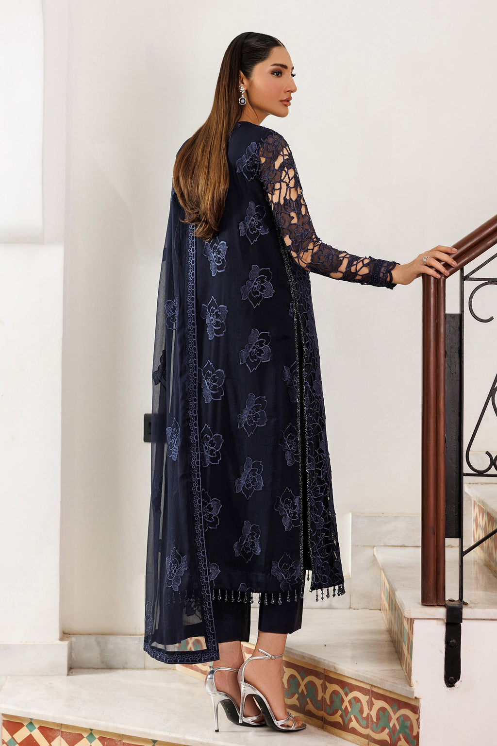 Woman in a navy blue embroidered outfit standing on a staircase.
