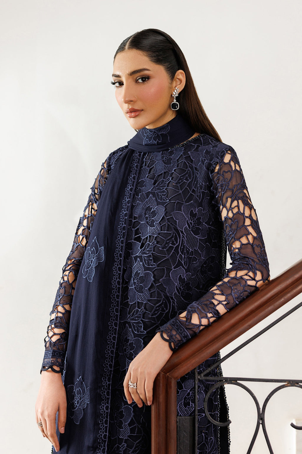 Woman wearing a navy lace dress standing against a white wall.