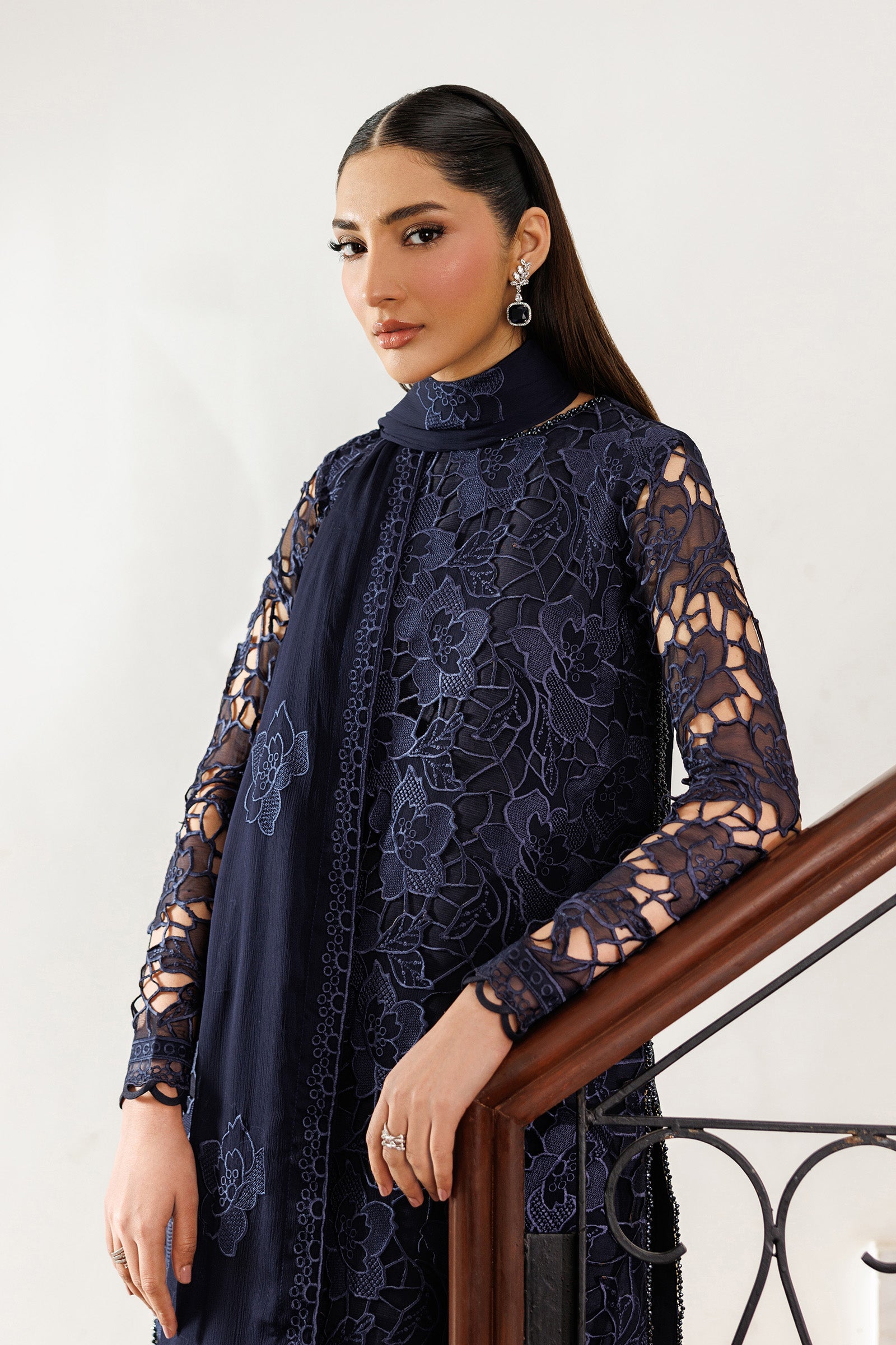 Woman wearing a navy lace dress standing against a white wall.