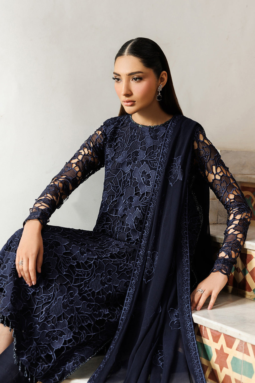 Woman wearing a dark blue lace outfit sitting on a white surface.