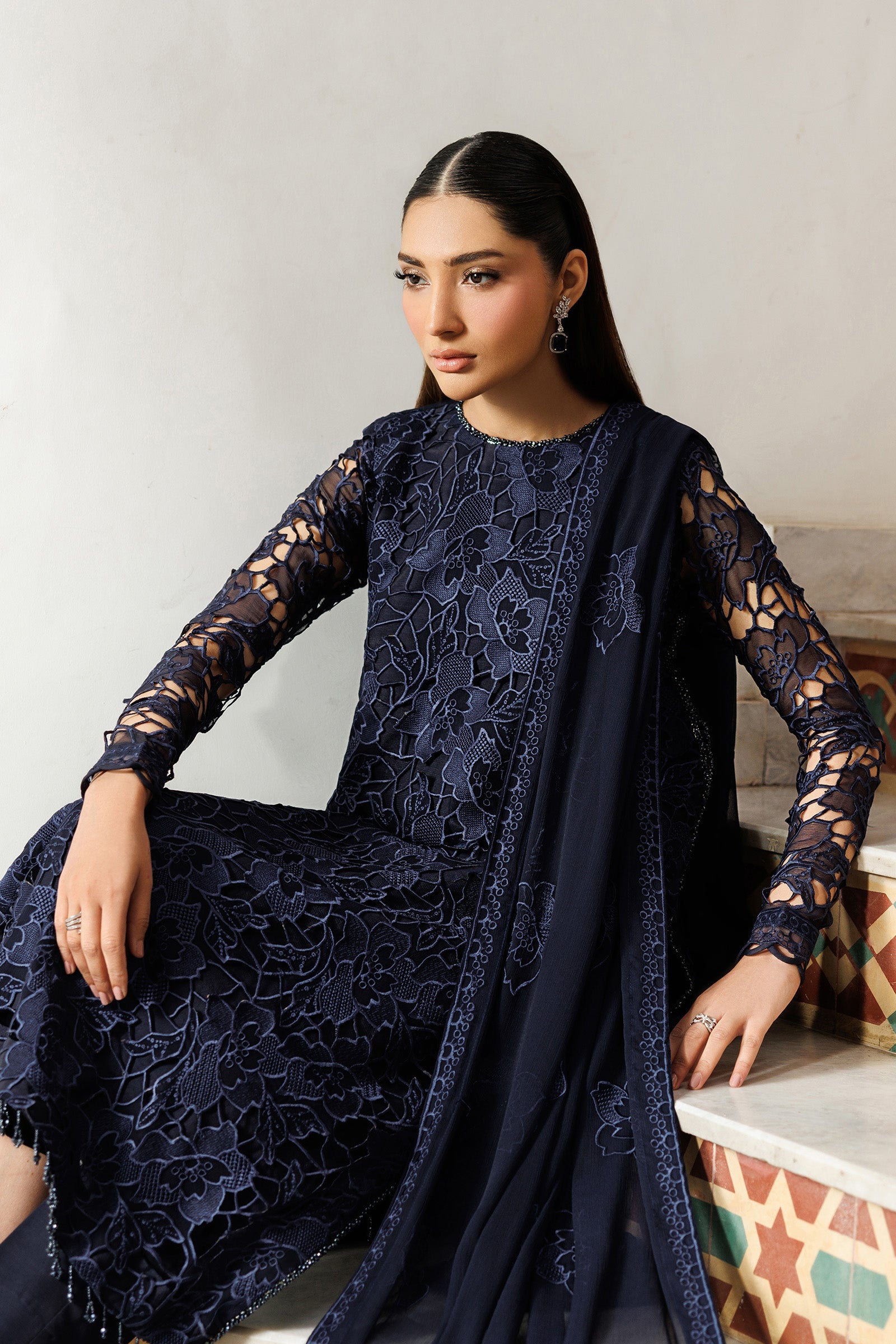 Woman wearing a dark blue lace outfit sitting on a white surface.