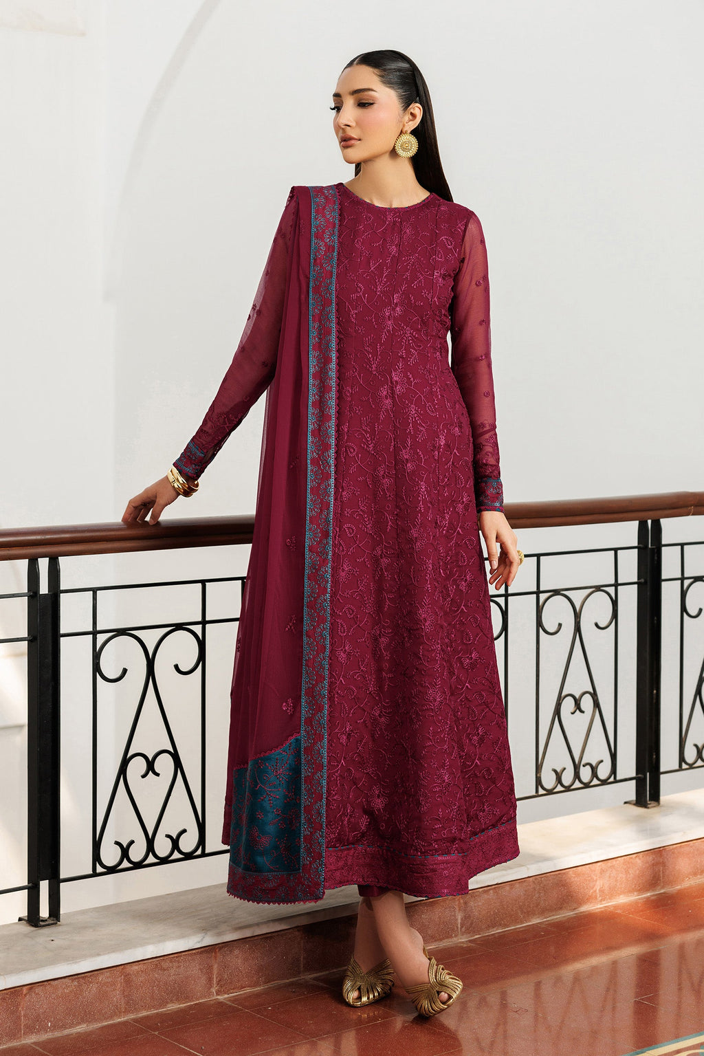 Woman in a maroon traditional outfit with a blue border standing indoors.
