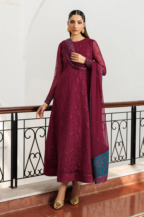 Woman in a maroon traditional outfit standing in an elegant interior setting.