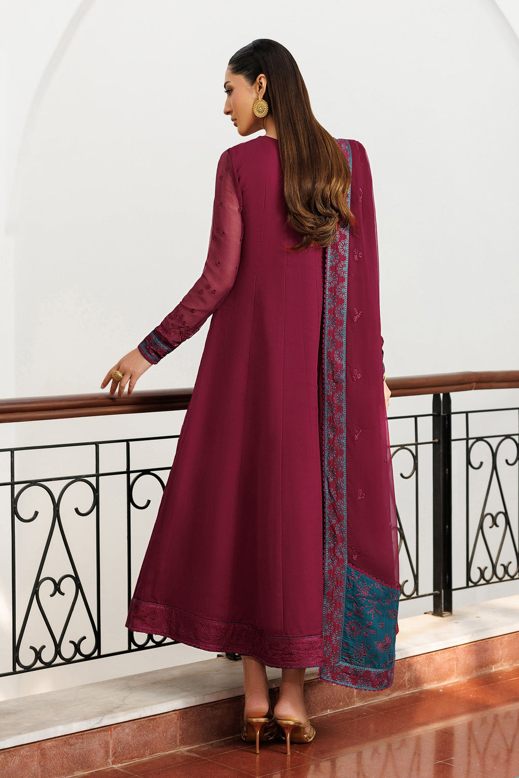 Woman in a long burgundy dress with a patterned scarf standing in an elegant interior setting.