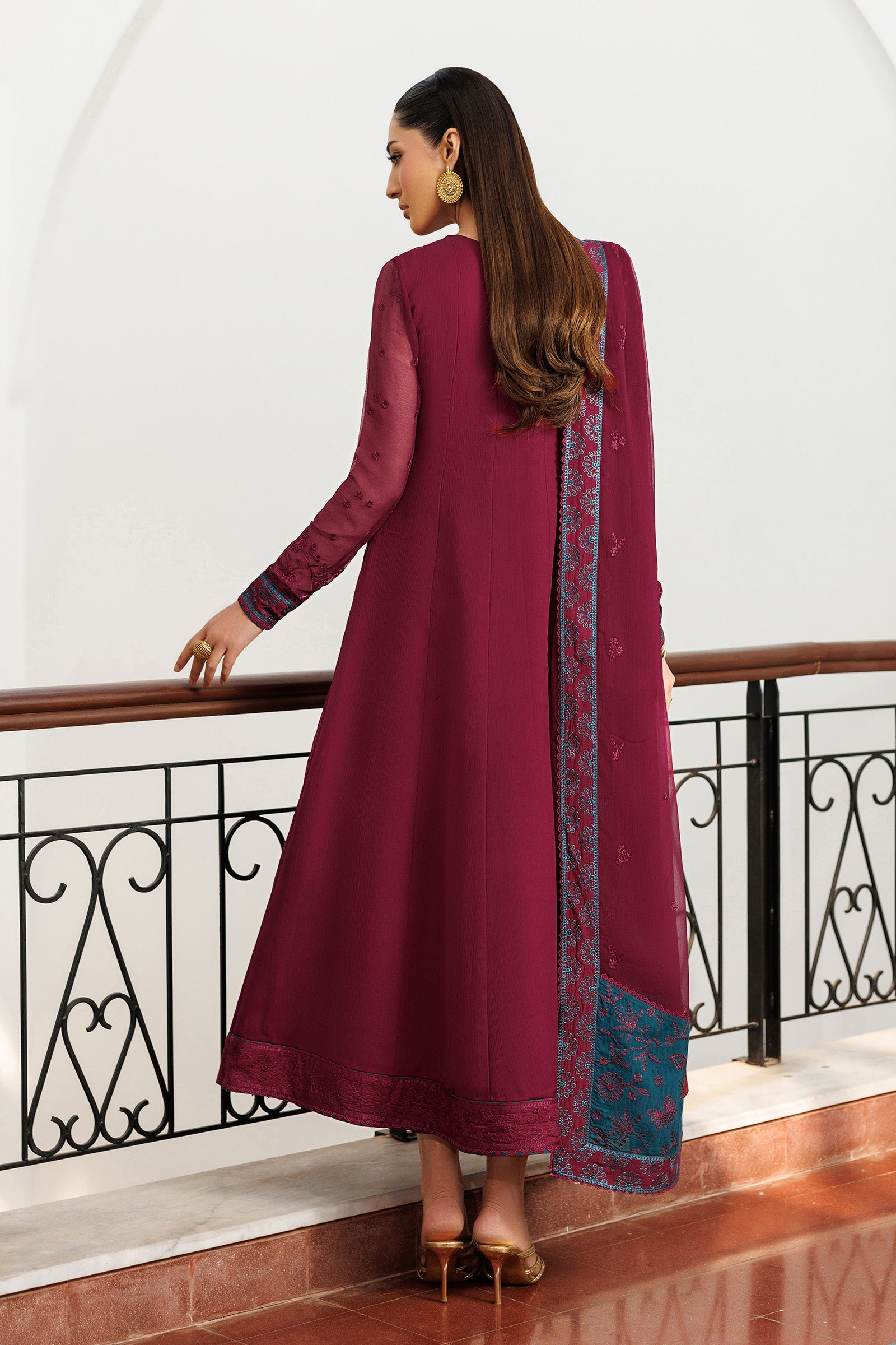 Woman in a long burgundy dress with a patterned scarf standing in an elegant interior setting.