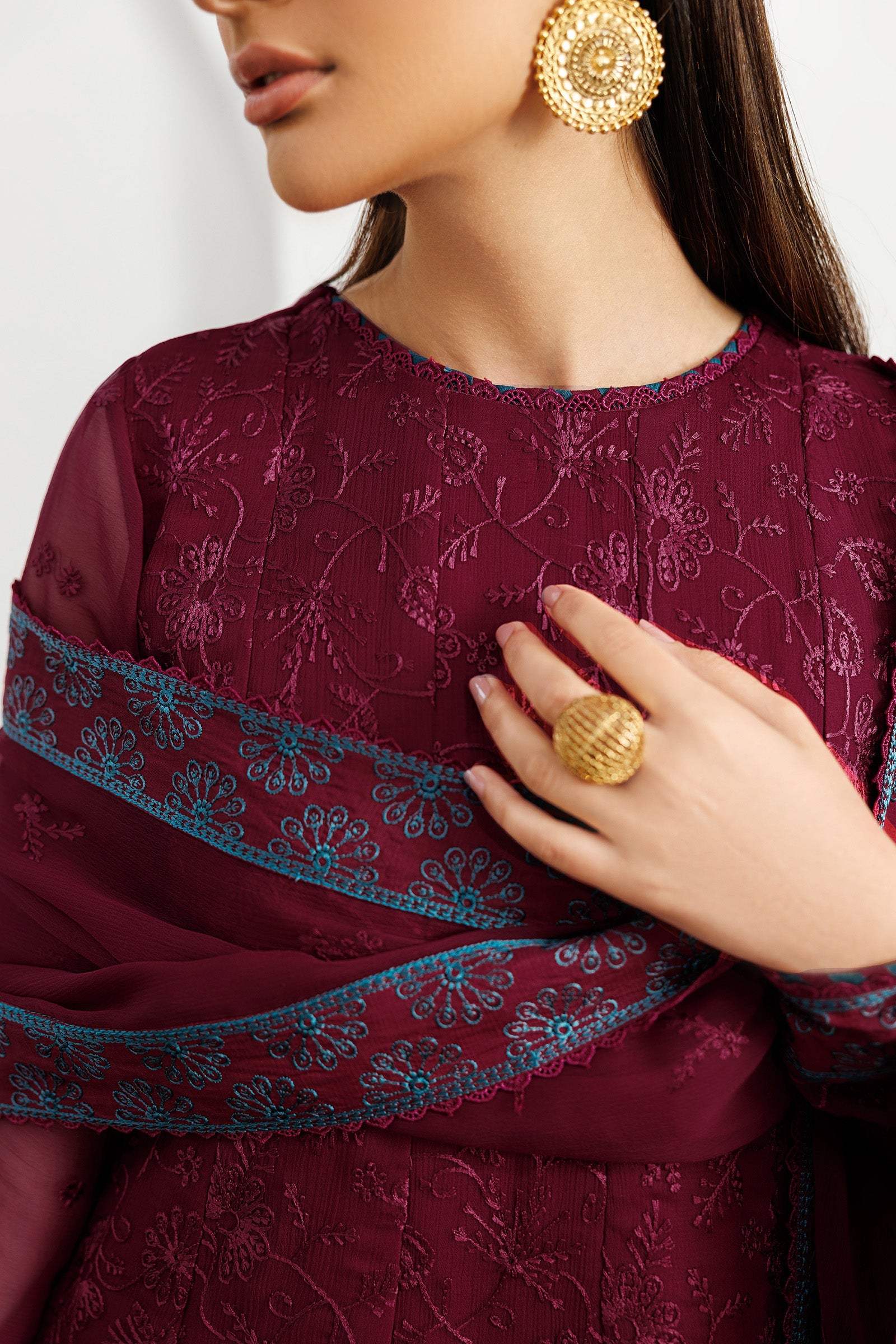 Close-up of a person wearing a maroon embroidered outfit with gold jewelry.