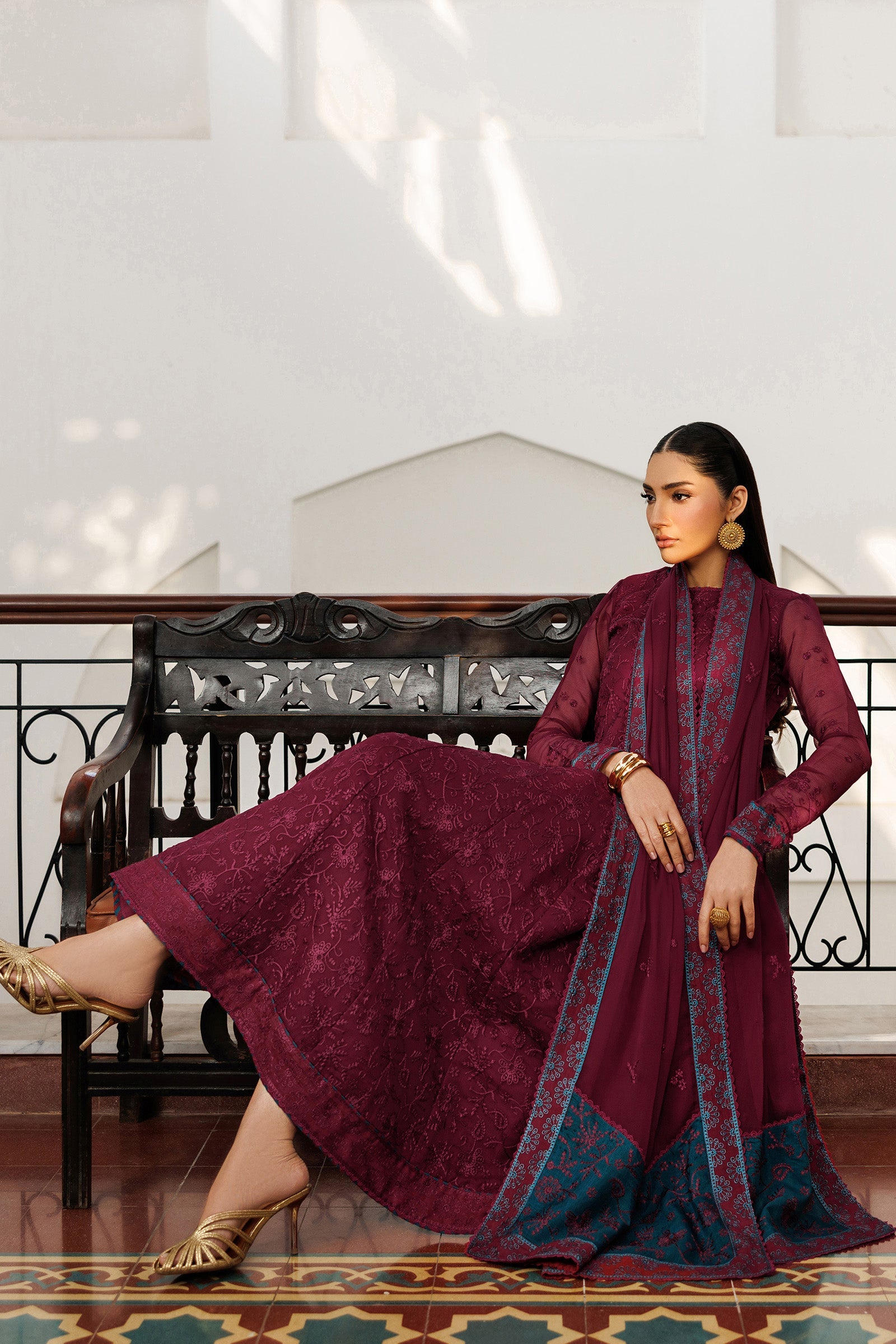 Woman in a maroon traditional outfit sitting on a decorative chair indoors.