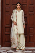 Woman in traditional white outfit with floral patterns standing in front of a wooden door.