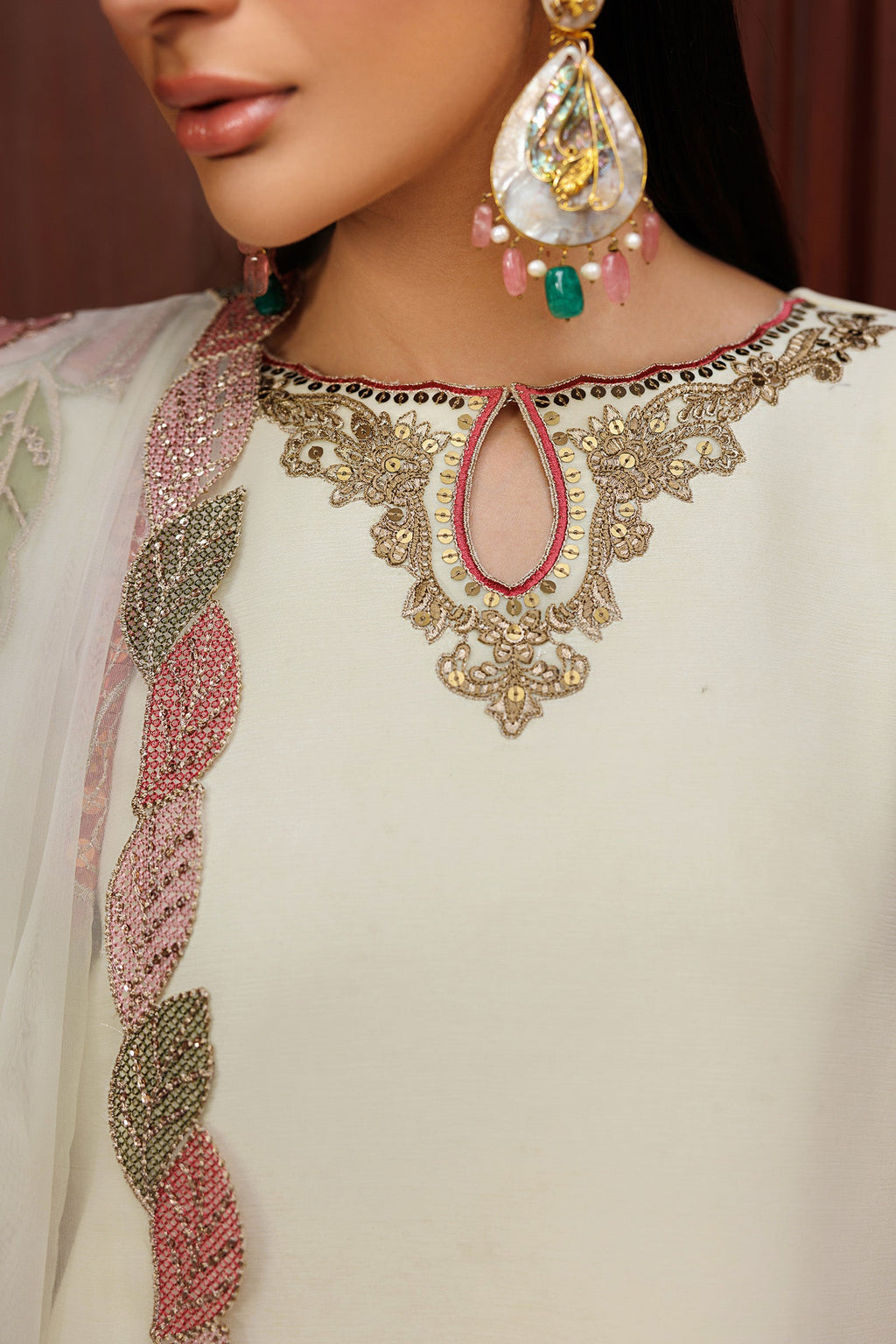 Close-up of a person wearing a white embroidered outfit with intricate designs and colorful jewelry.