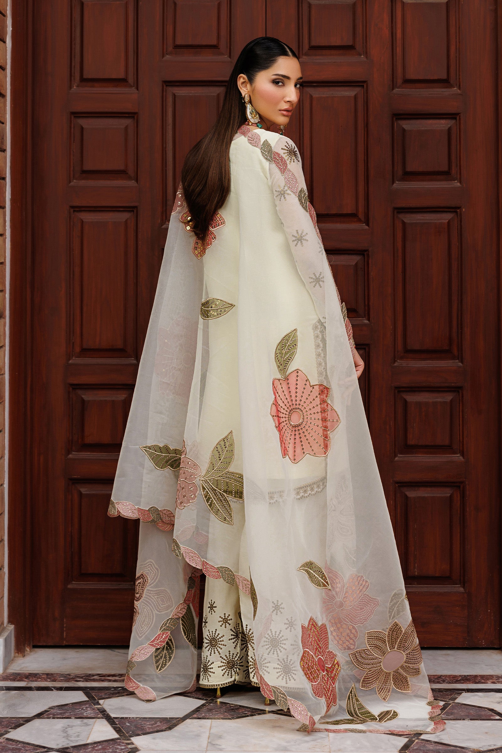Woman wearing a white embroidered outfit in front of a wooden door.