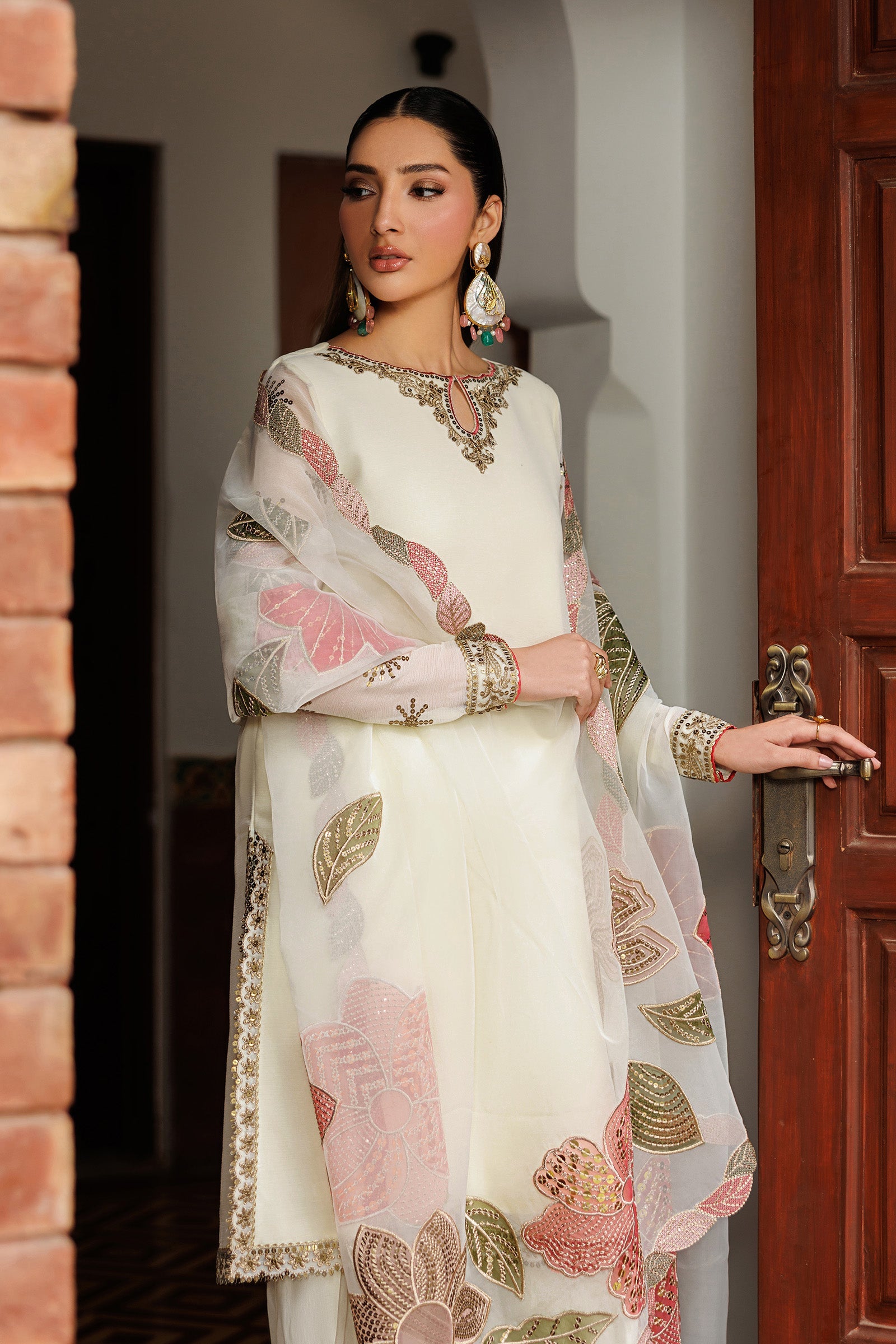 Woman in a traditional outfit with floral patterns standing in front of a wooden door.