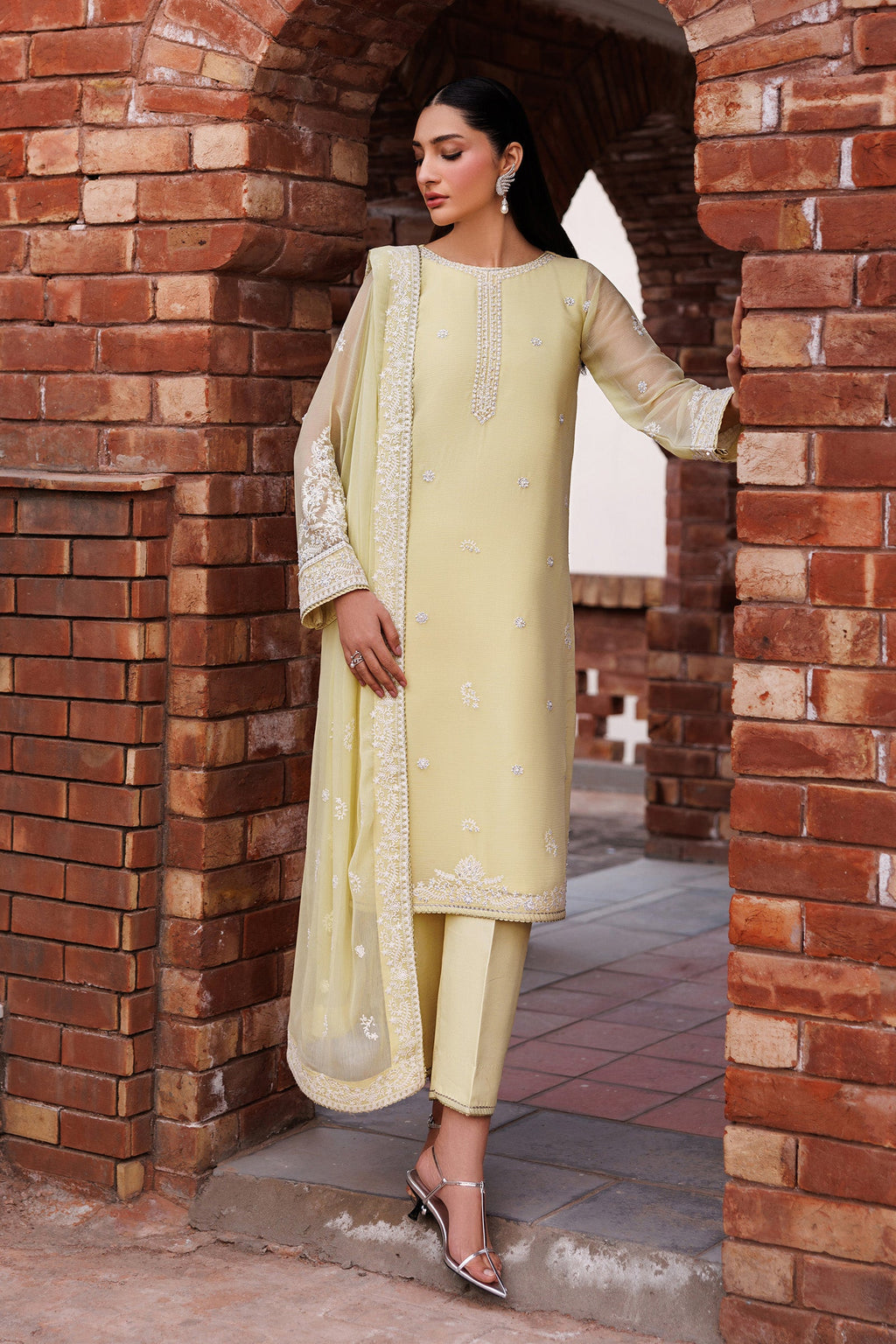 Woman in a light yellow traditional outfit standing in front of a brick archway.