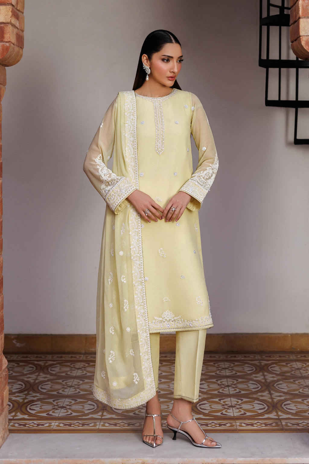 Woman wearing a light yellow traditional outfit with intricate patterns in a room with a patterned floor.