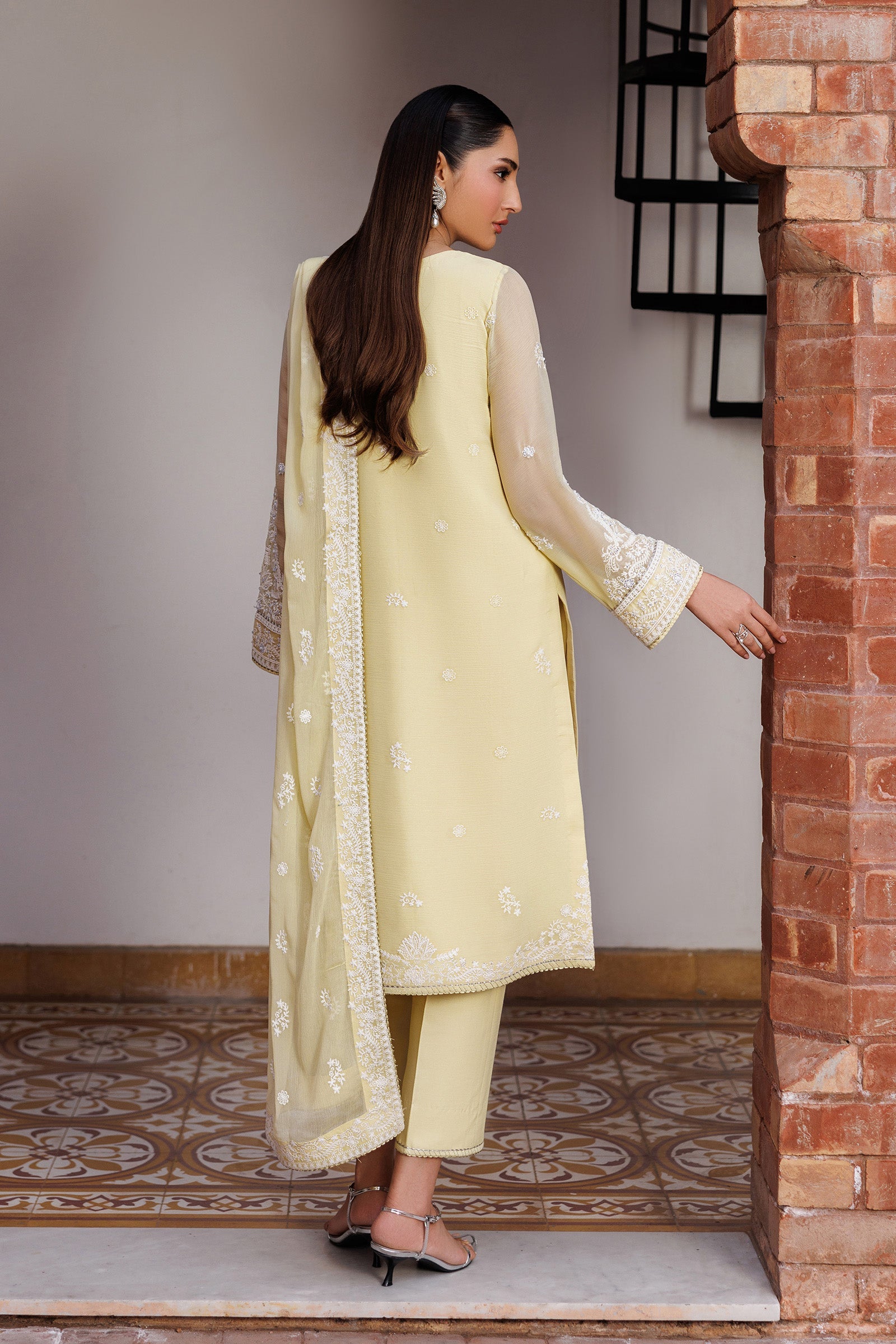 Woman in a light yellow traditional outfit standing in a doorway.