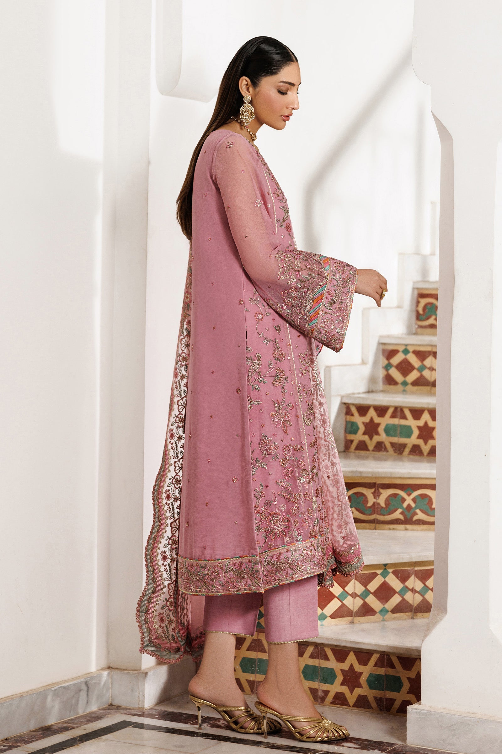 Woman in a pink traditional outfit standing in a decorative interior setting.