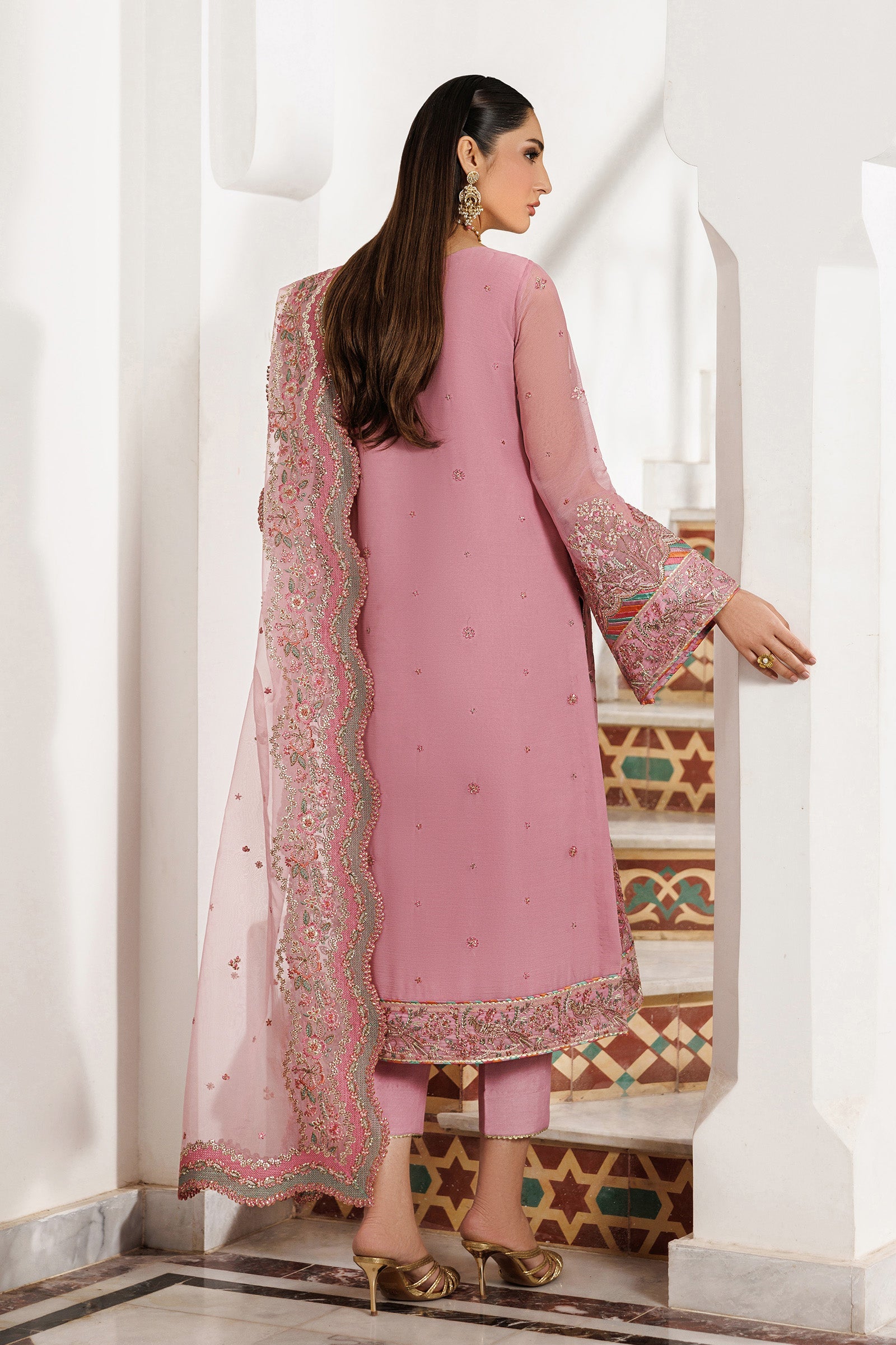 Woman wearing a pink traditional outfit with a matching dupatta in a decorative interior setting.