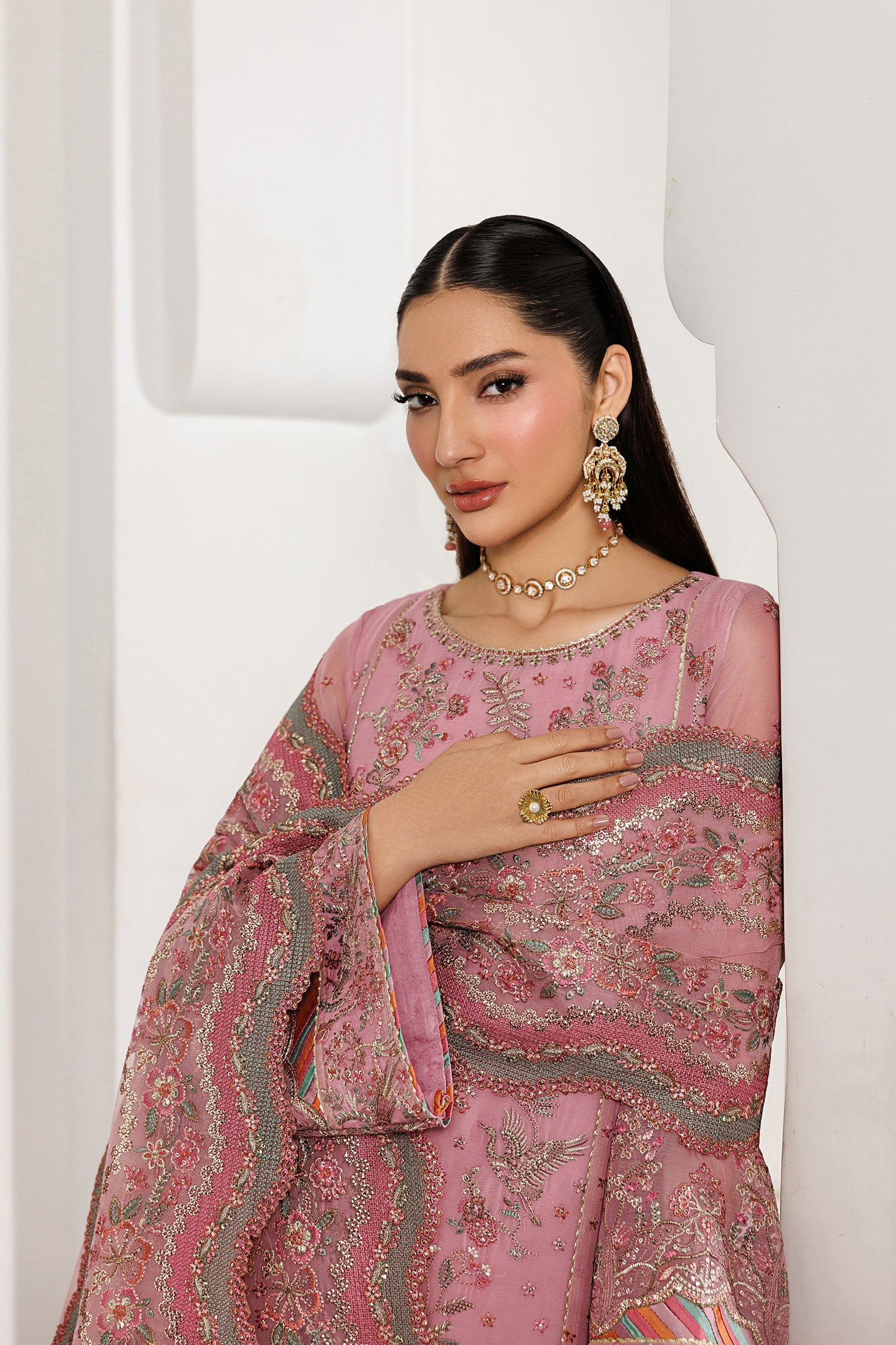 Woman wearing a pink embroidered traditional outfit with jewelry against a white background
