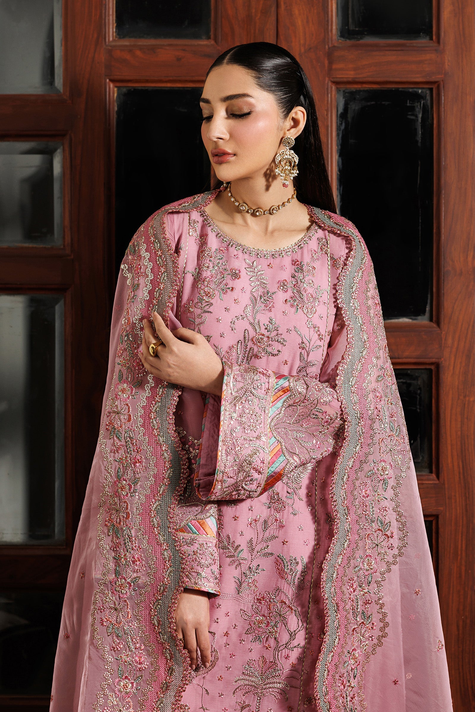 Woman wearing a pink embroidered traditional outfit with a wooden door in the background