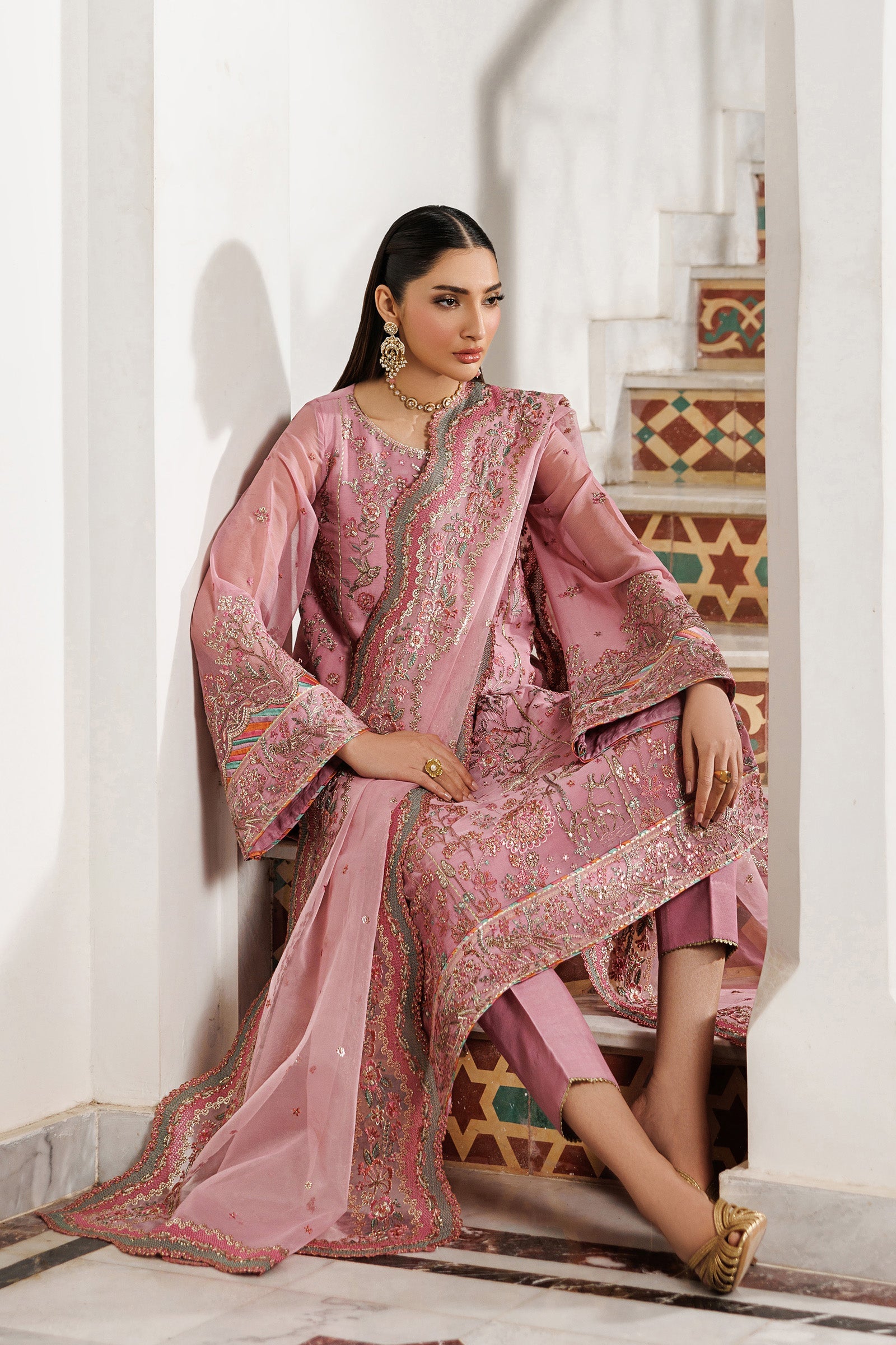 Woman in a traditional pink embroidered outfit sitting on a staircase.