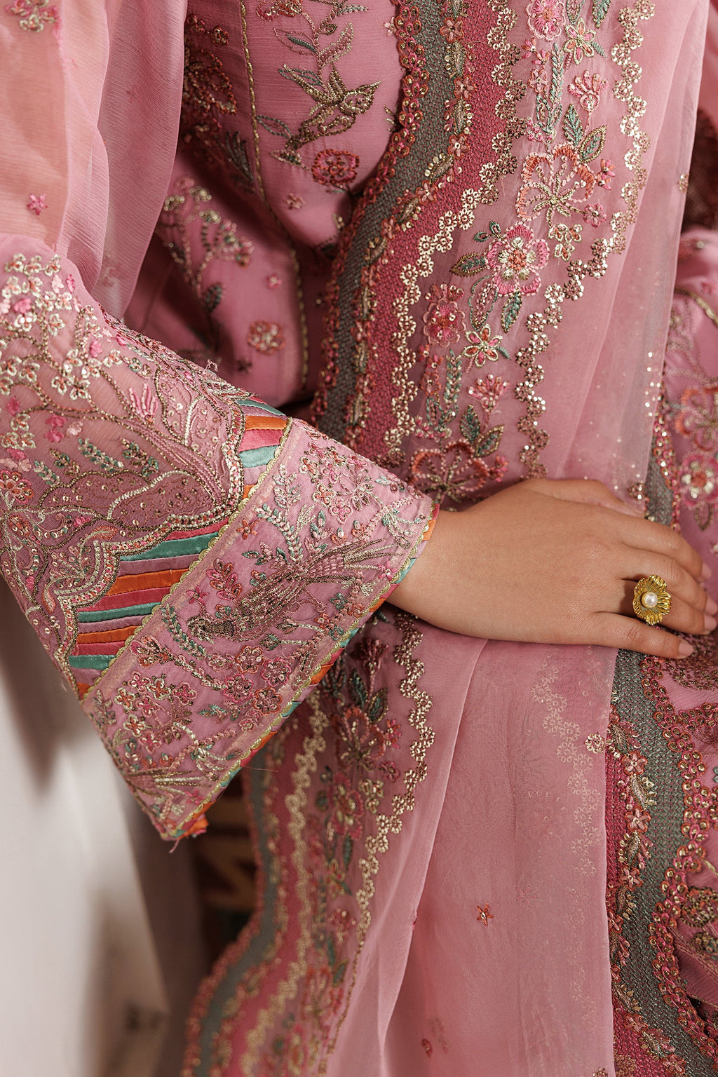 Close-up of a pink embroidered garment with intricate patterns and a hand wearing a ring.