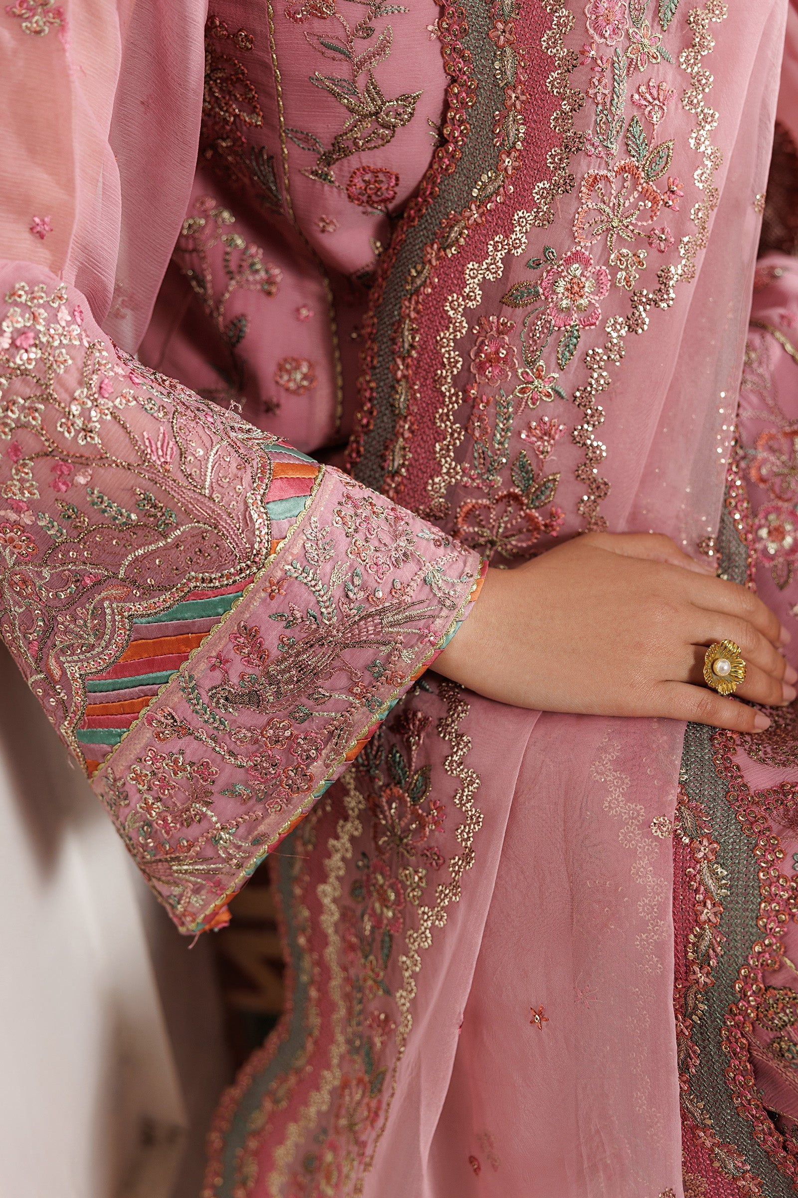 Close-up of a pink embroidered garment with intricate patterns and a hand wearing a ring.