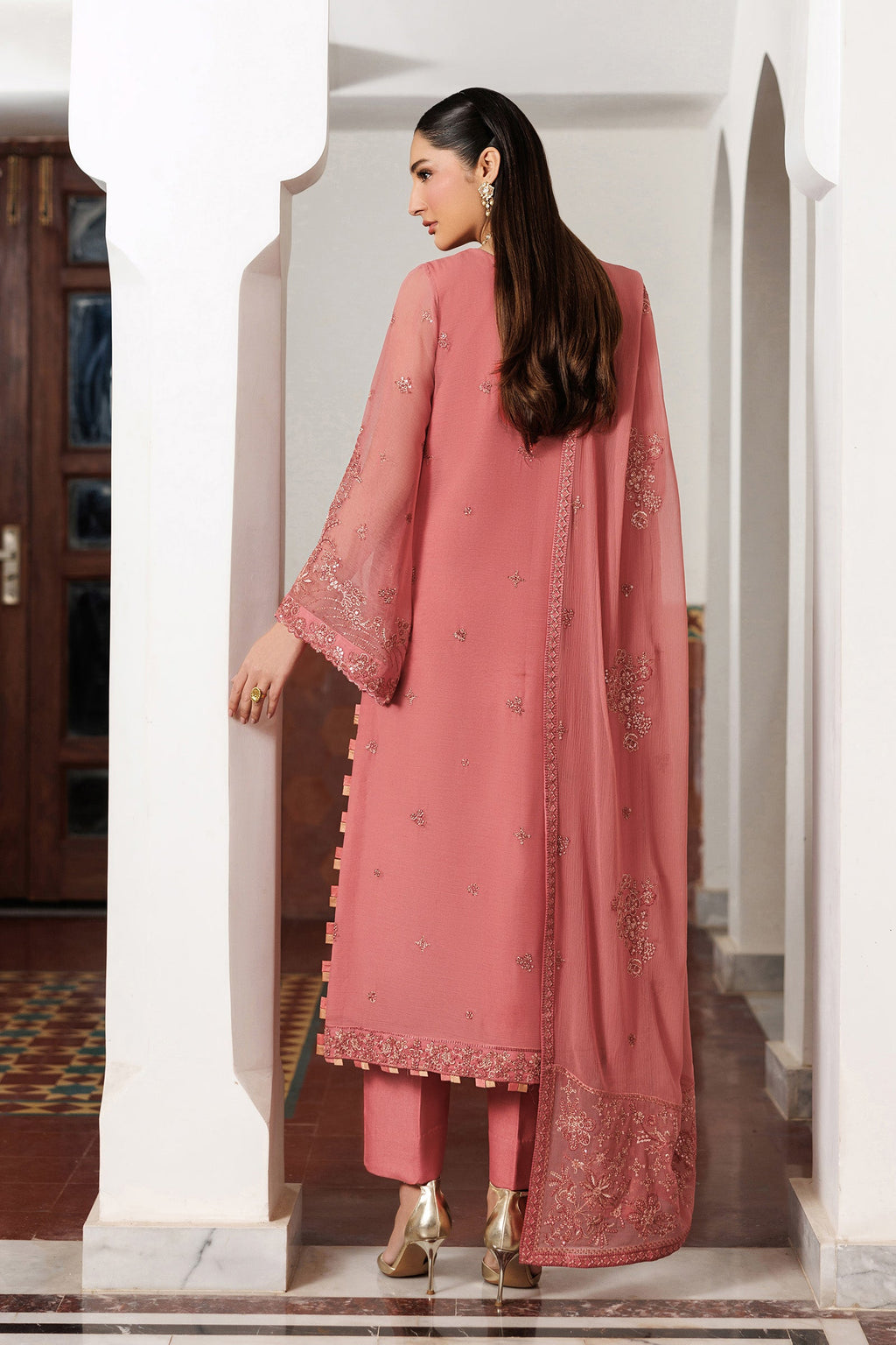 Woman in a pink traditional outfit with lace details standing in a doorway.