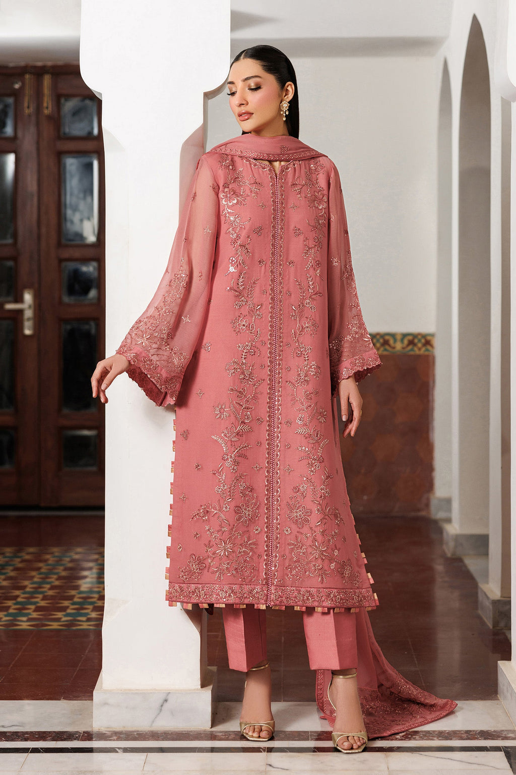 Woman in a pink embroidered traditional outfit standing indoors.