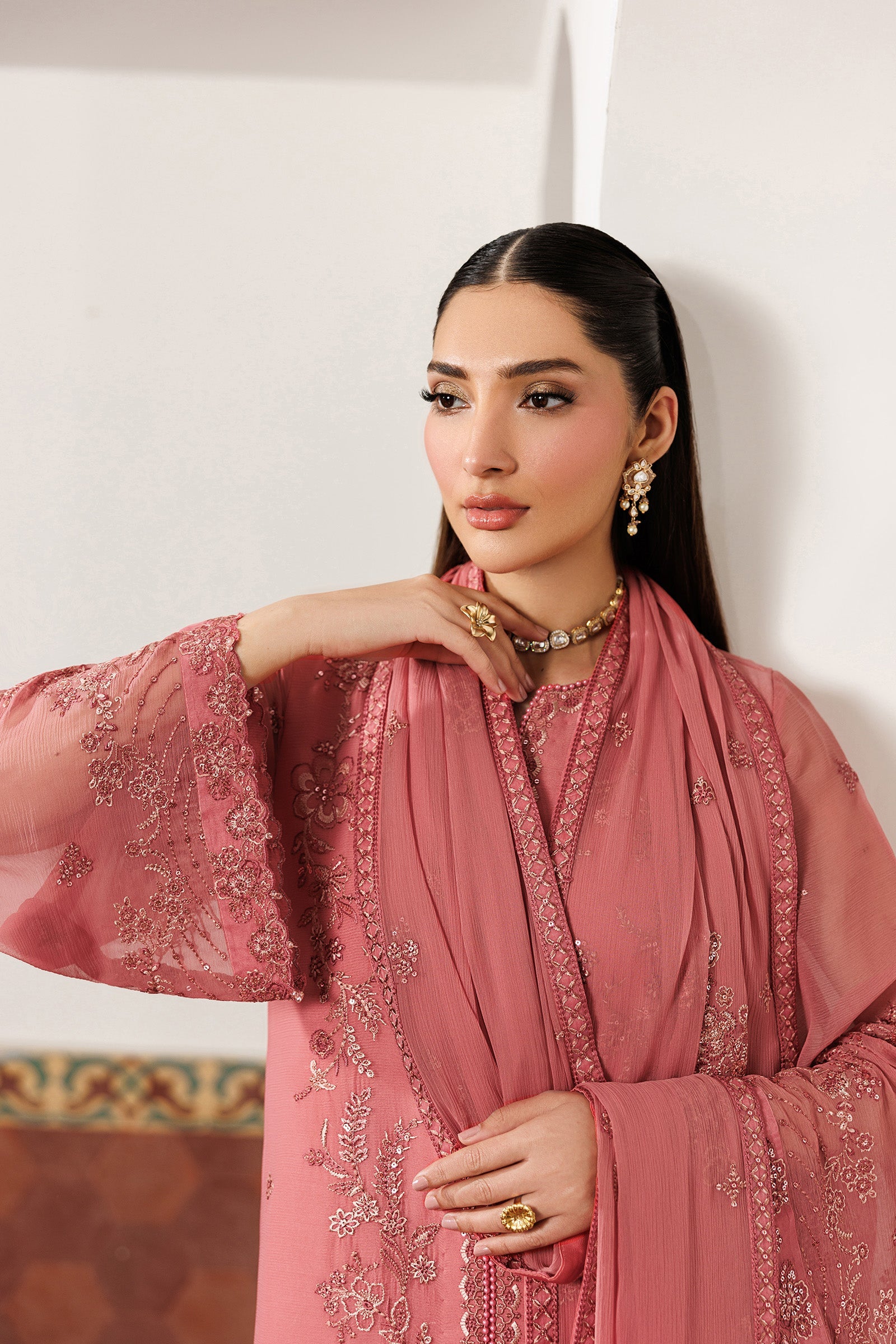 Woman wearing a pink embroidered traditional outfit against a white wall.