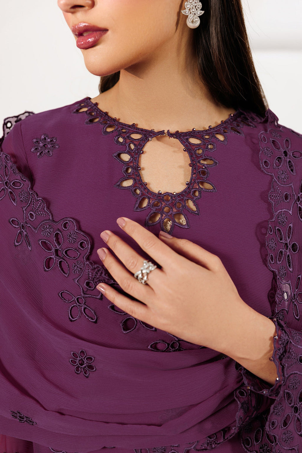 Purple embroidered dress with floral patterns and a hand wearing a ring.