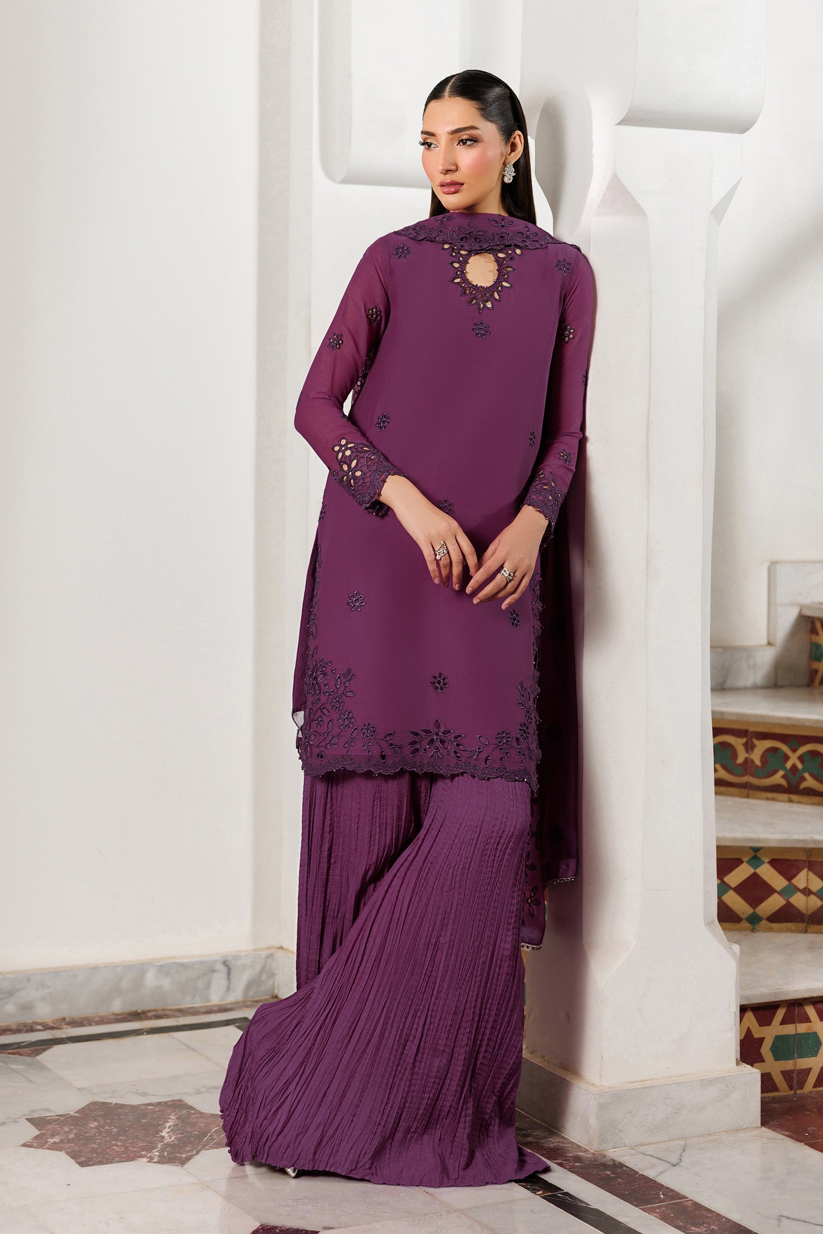 Woman wearing a purple traditional outfit with intricate designs in a decorative interior setting.