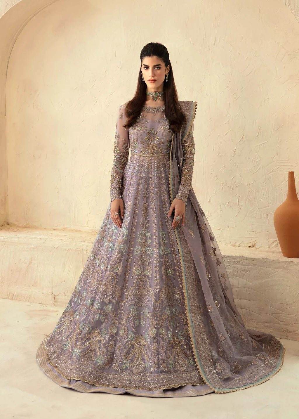 Woman in a gray embroidered gown standing against a beige wall.